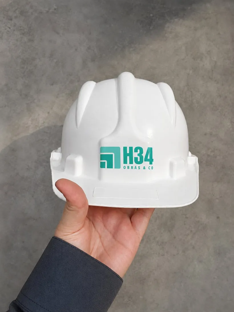 Casco de obra blanco con el logo de H34 sostenido en una mano